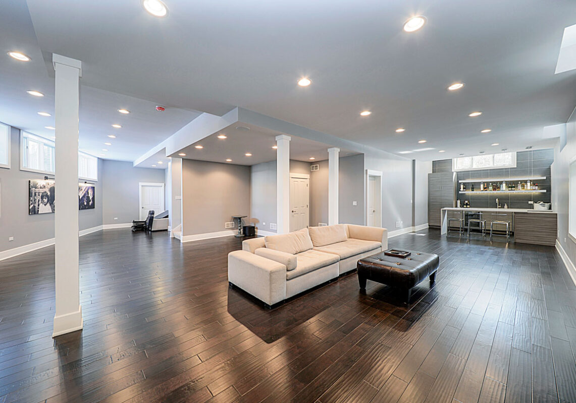 Basement remodeling with open living area, dark flooring, and custom bar