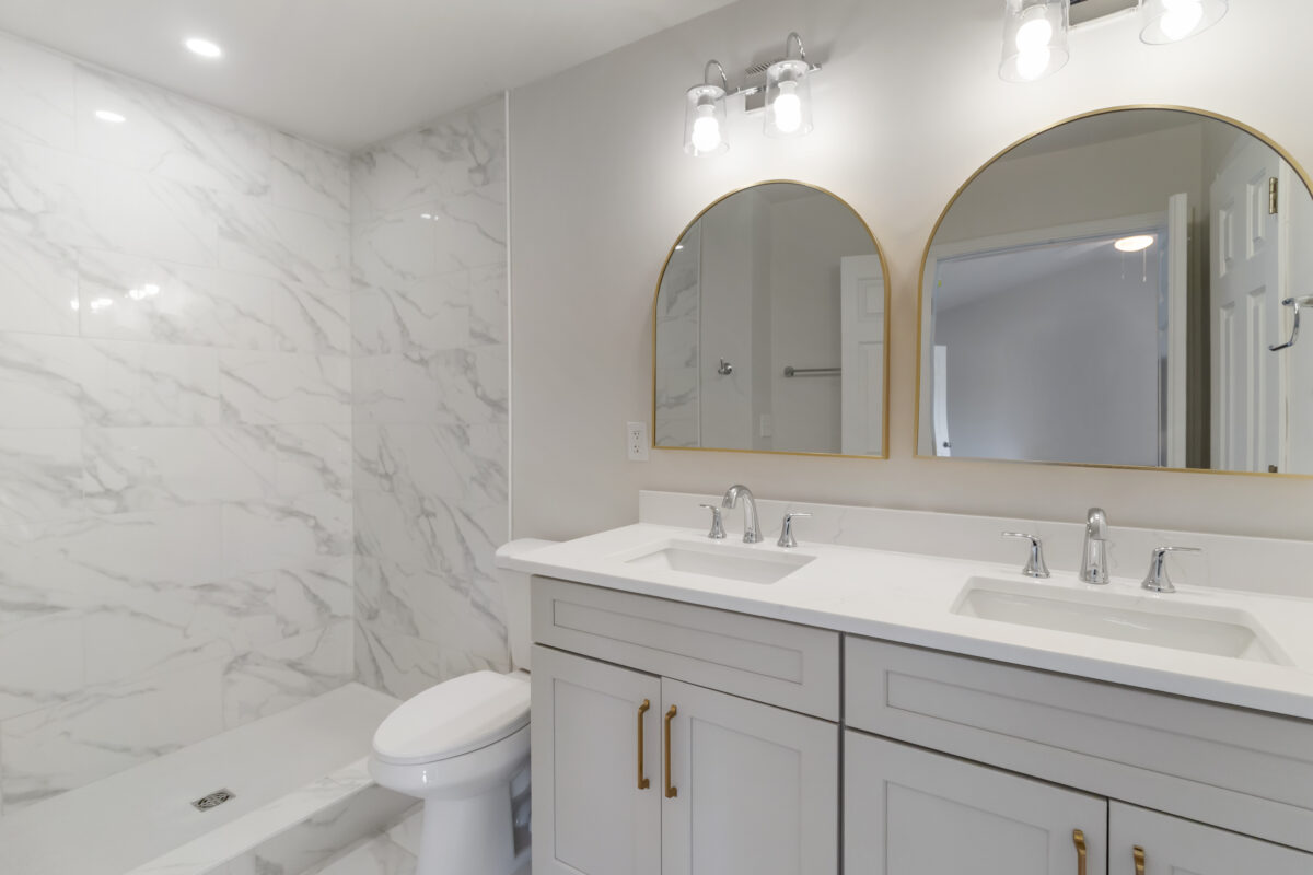 Modern bathroom featuring marble walls, a double-sink vanity, and two arched mirrors above the counter.