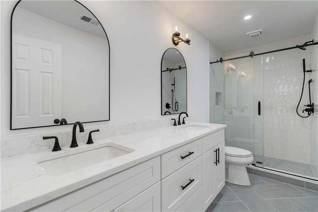 White bathroom with a double vanity, marble countertop, black faucets, and large arched mirrors.