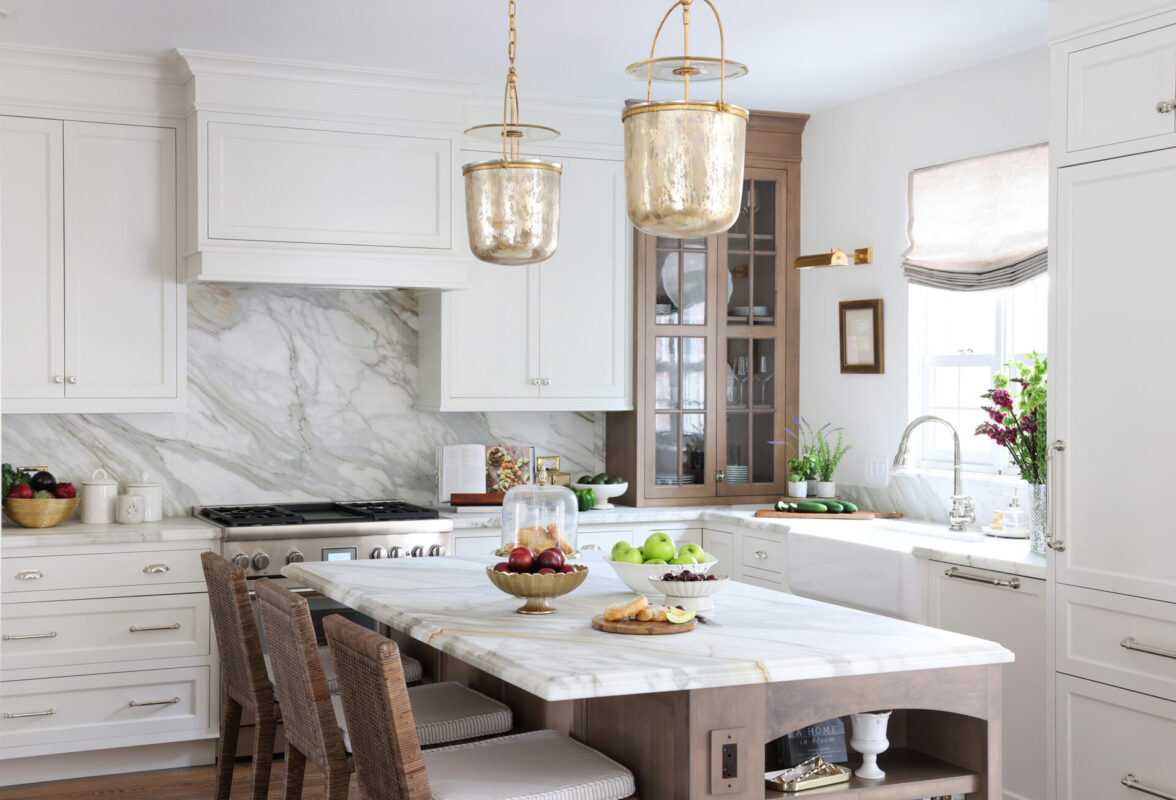 Bright white kitchen with marble backsplash and island, gold pendant lights, and fruit bowls on the counter