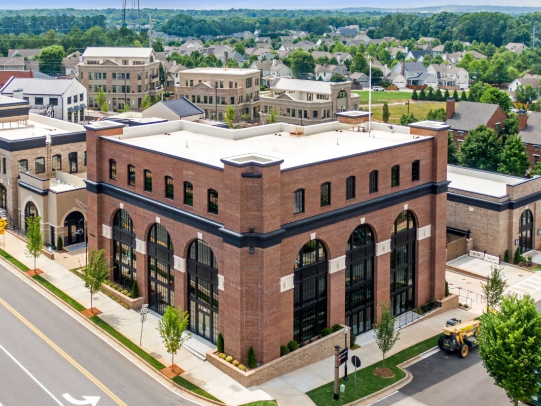 Aerial view of a brick multi-story building with large arched windows and a white rooftop edge, in a developing urban area.