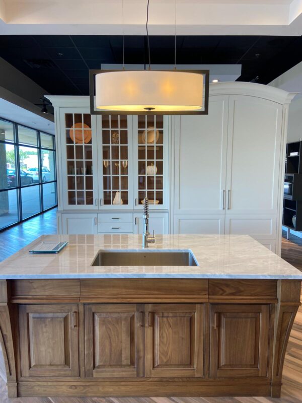 Modern showroom kitchen: wood island with marble countertop, undermount sink and spring faucet, white cabinetry with glass-front doors, and a large pendant light above