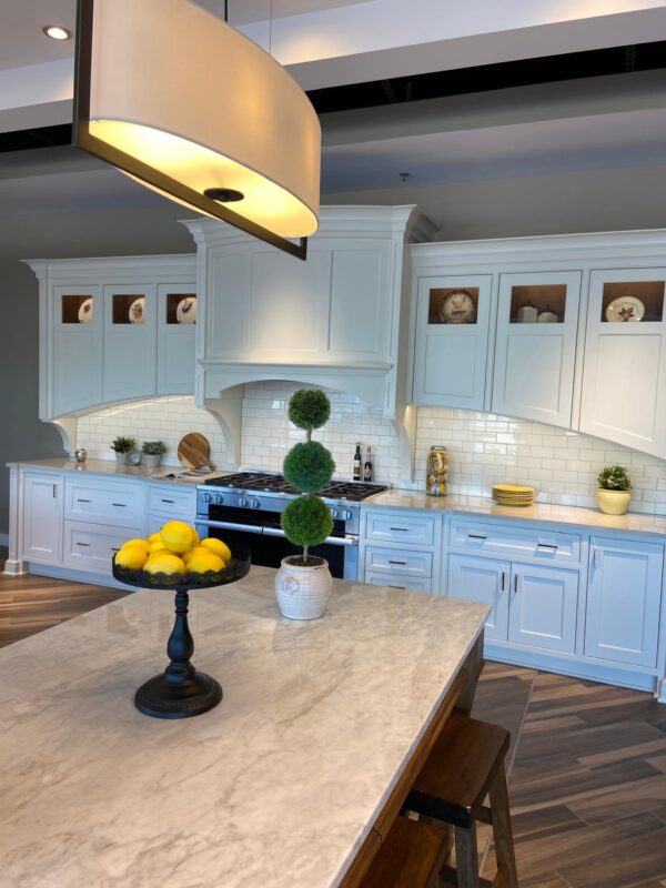 Bright white kitchen with a marble island, topiary plant, and a lemon bowl in the foreground.