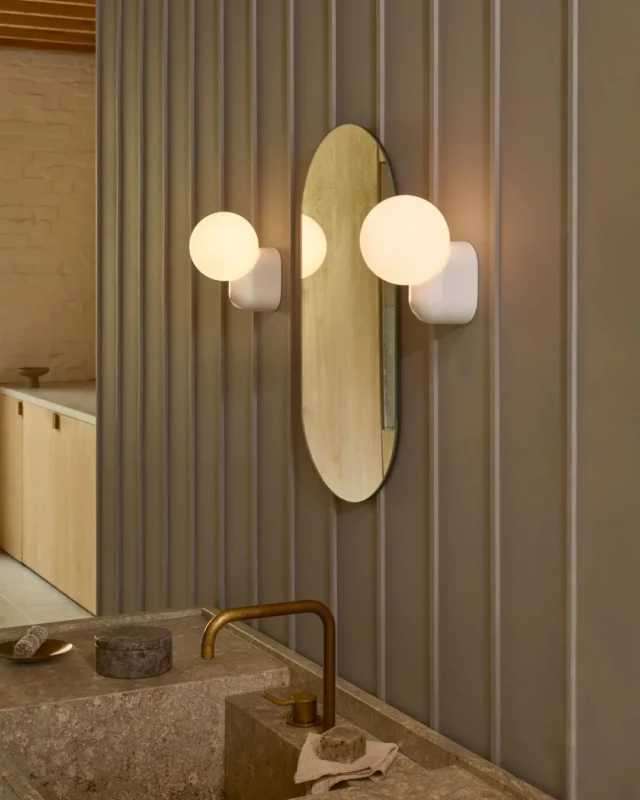 Modern bathroom with vertical panel walls, an oval mirror, and two spherical wall sconces flanking the mirror.