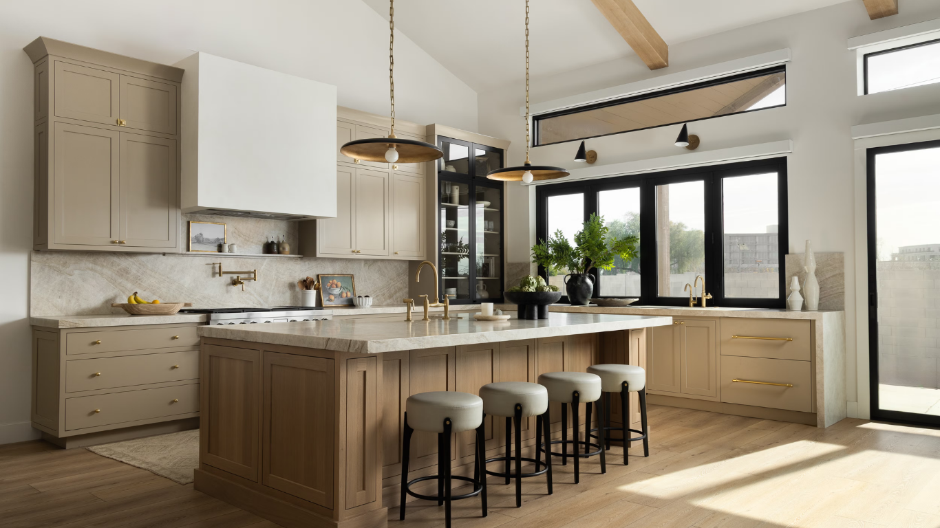 Modern kitchen with a large island, beige cabinetry, and a marble countertop under warm pendant lights. Four cushioned stools line the island.